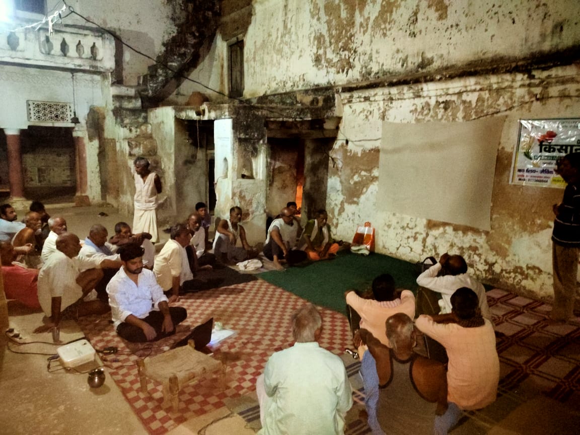 Farmers seated for an evening meeting in a village courtyard